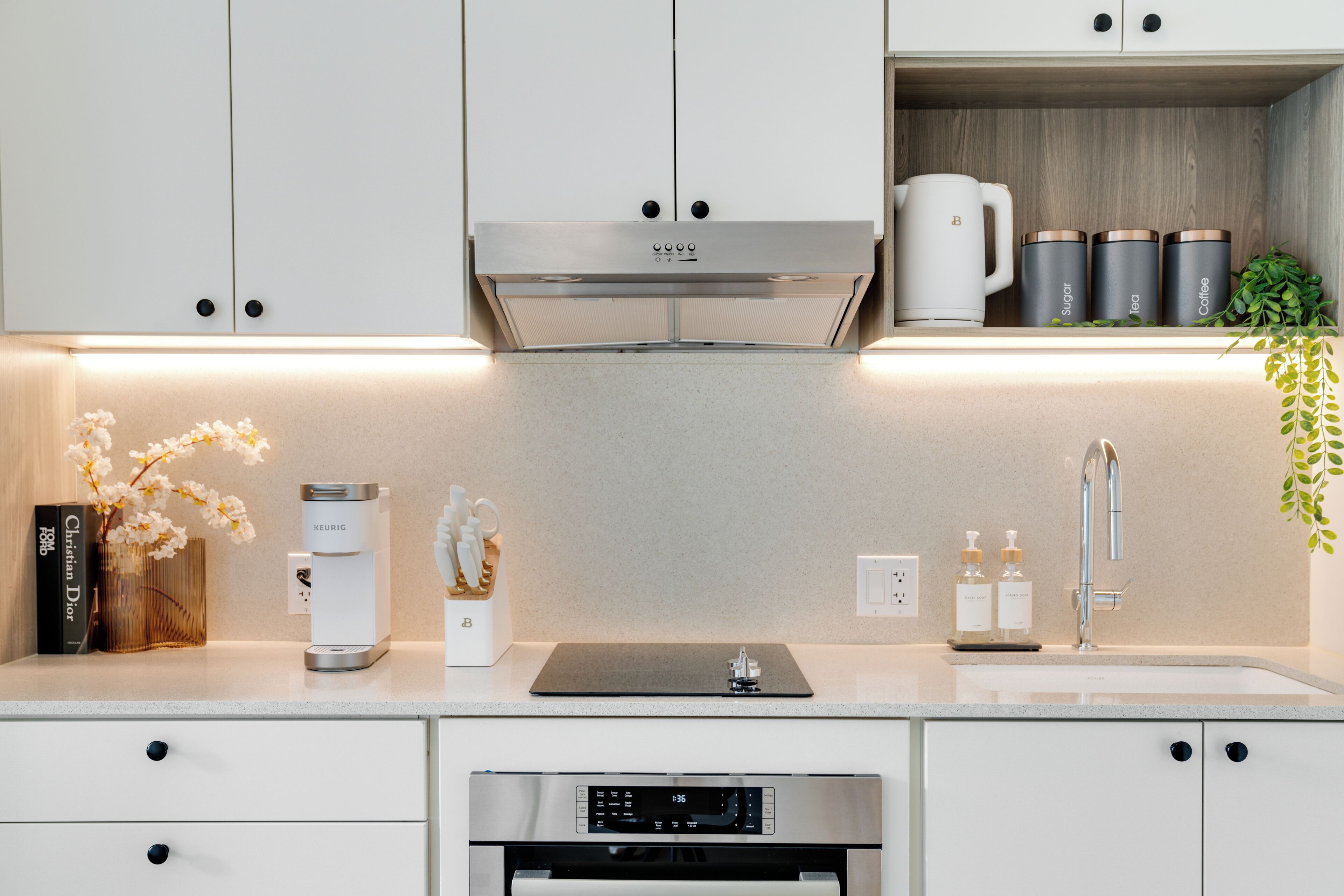 Una cocina moderna con armarios blancos, horno empotrado, cafetera y lavabo.