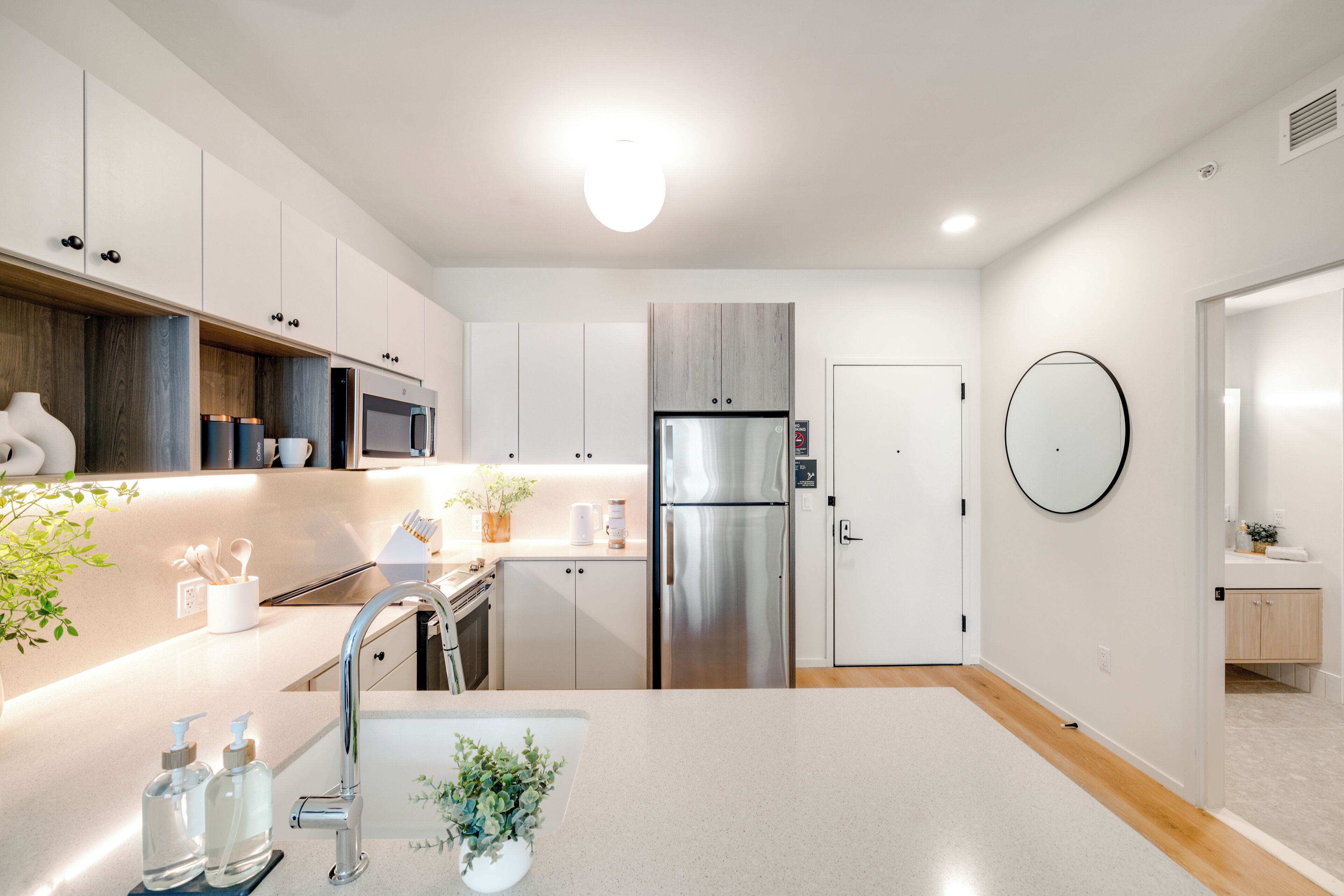 A modern kitchen with white cabinets, stainless steel appliances, and a central island with a sink and plant.