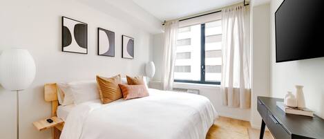 A modern hotel room with a large bed, a desk, and a flat-screen TV.