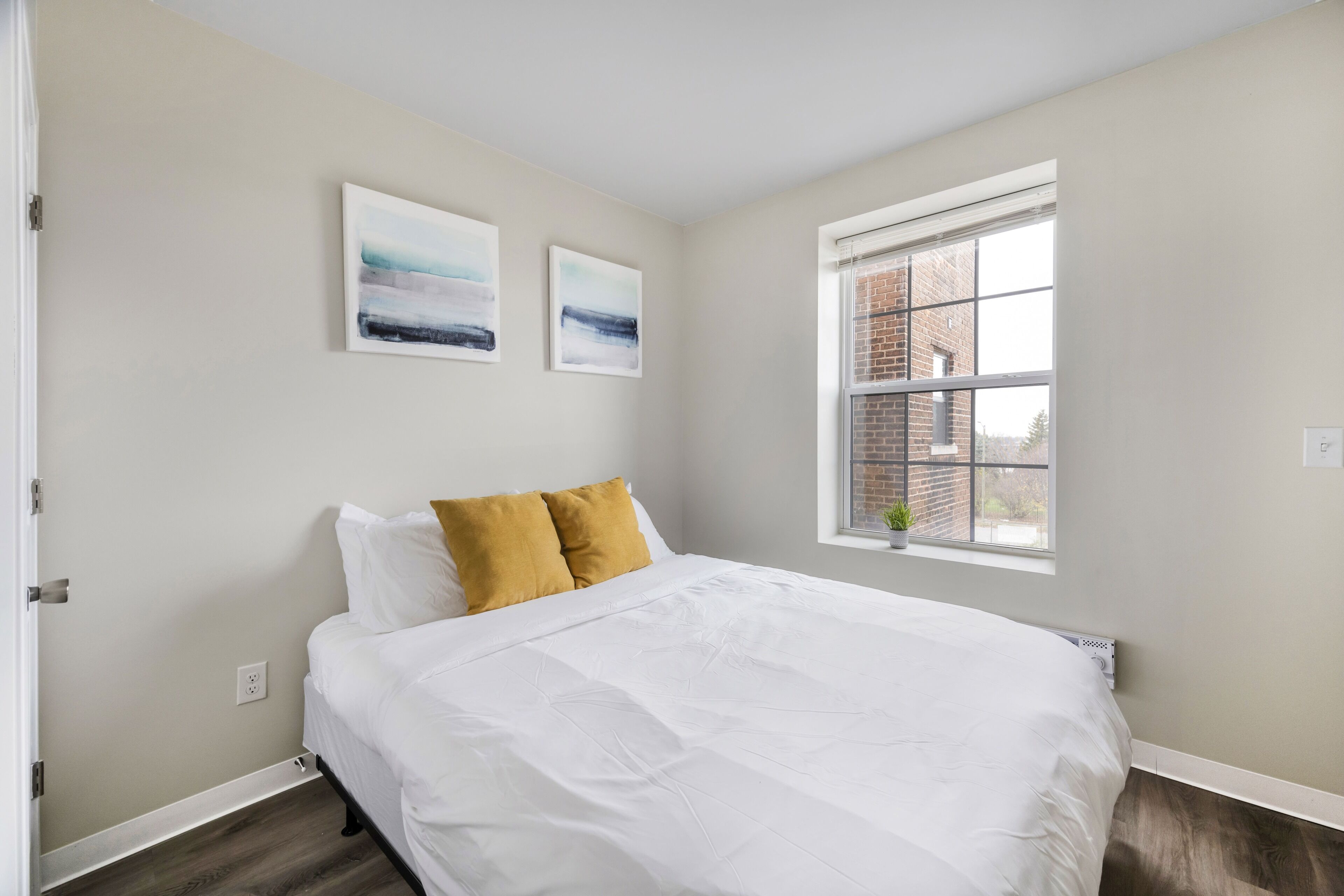 A bedroom with a bed, two pillows, a window, and two wall-mounted artworks.