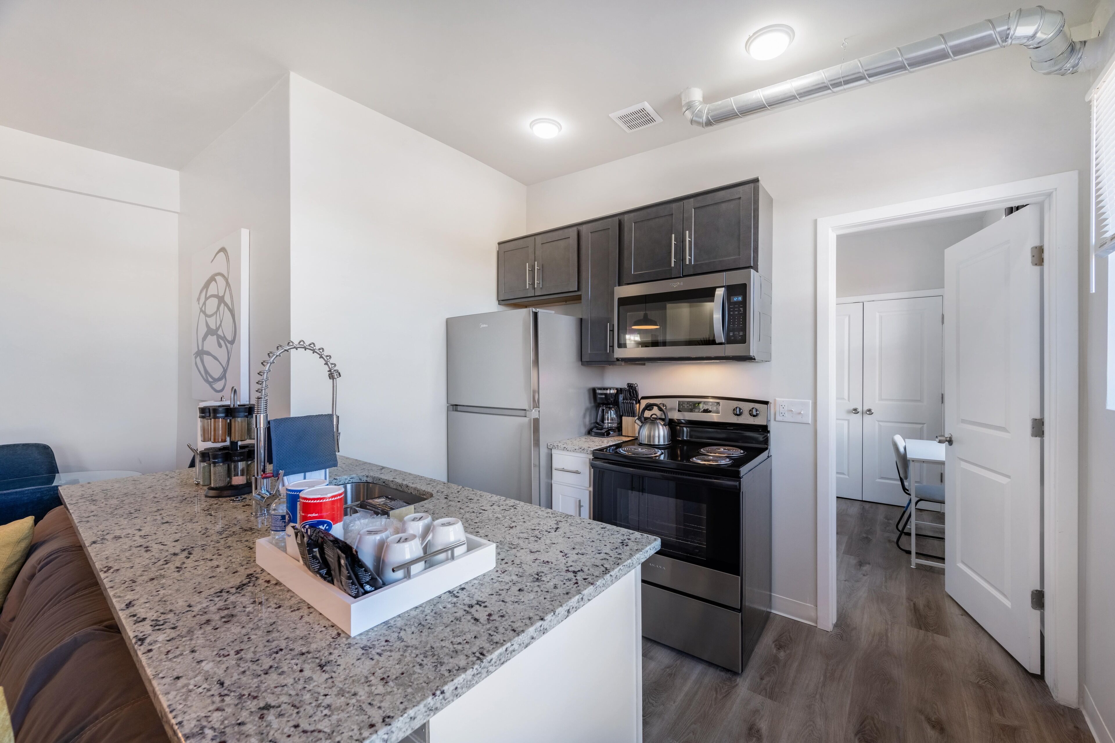 A modern kitchen with granite countertops, stainless steel appliances, and a central island with a coffee machine and tea kettle.