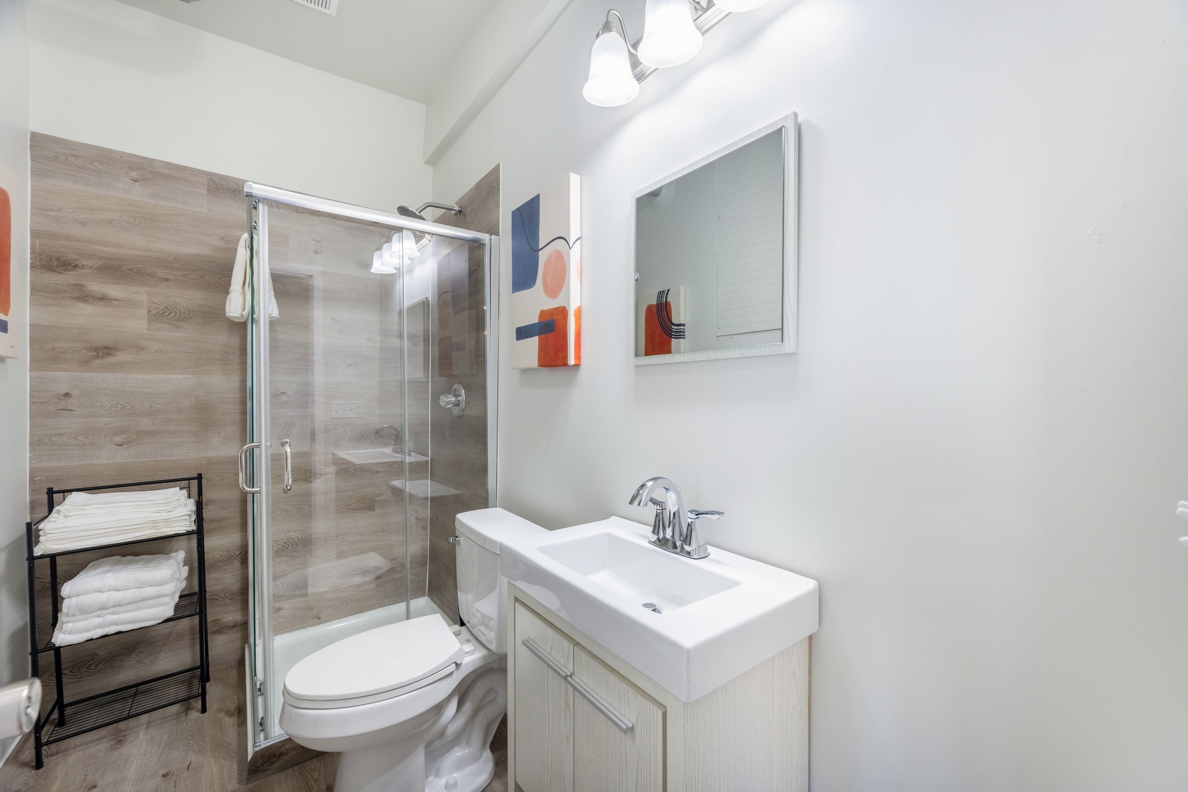A modern bathroom with a glass shower enclosure, a white toilet, and a white sink with a cabinet.