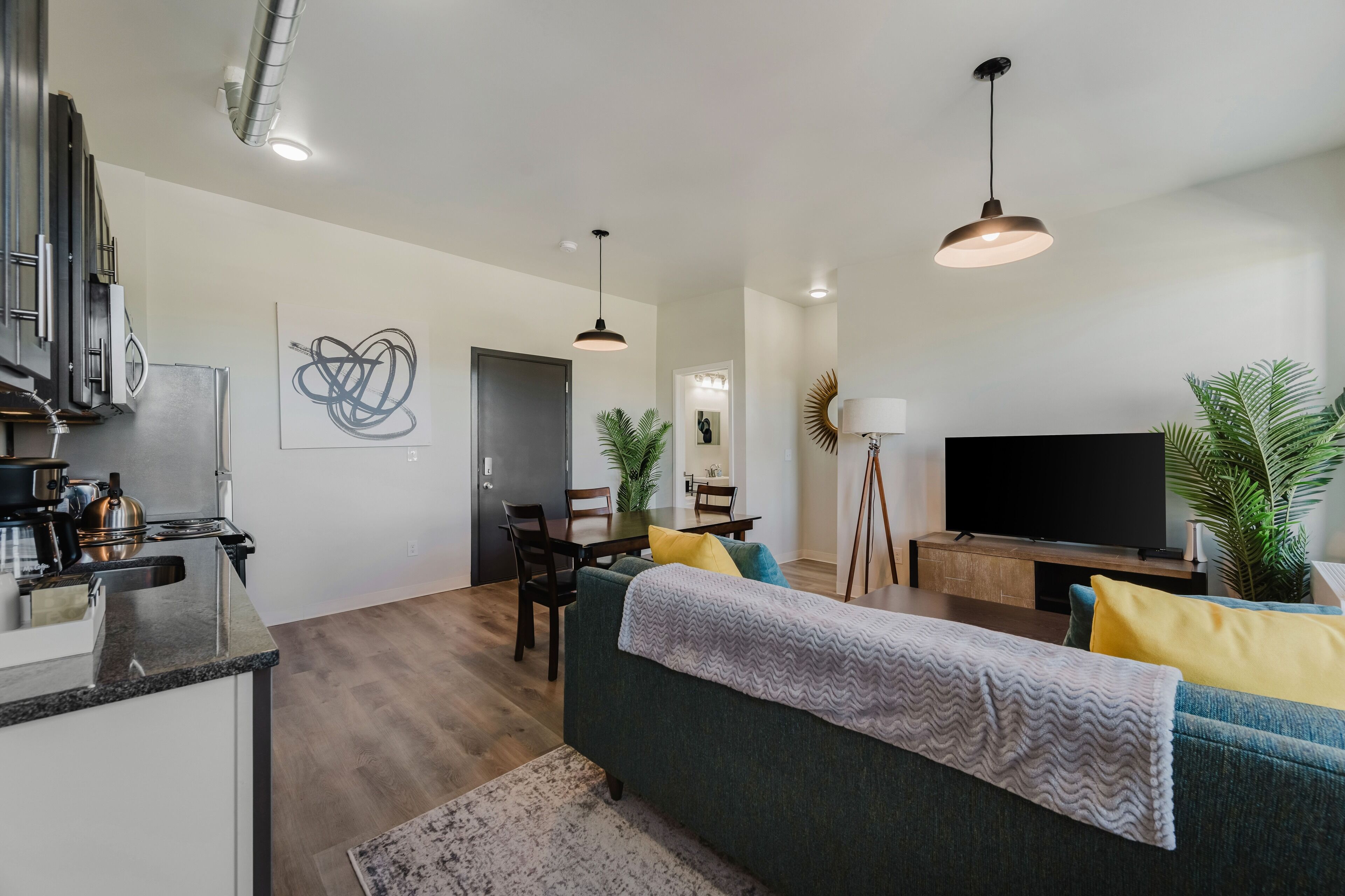 Una sala moderna con sofá, televisor, mesa de comedor y zona de cocina.