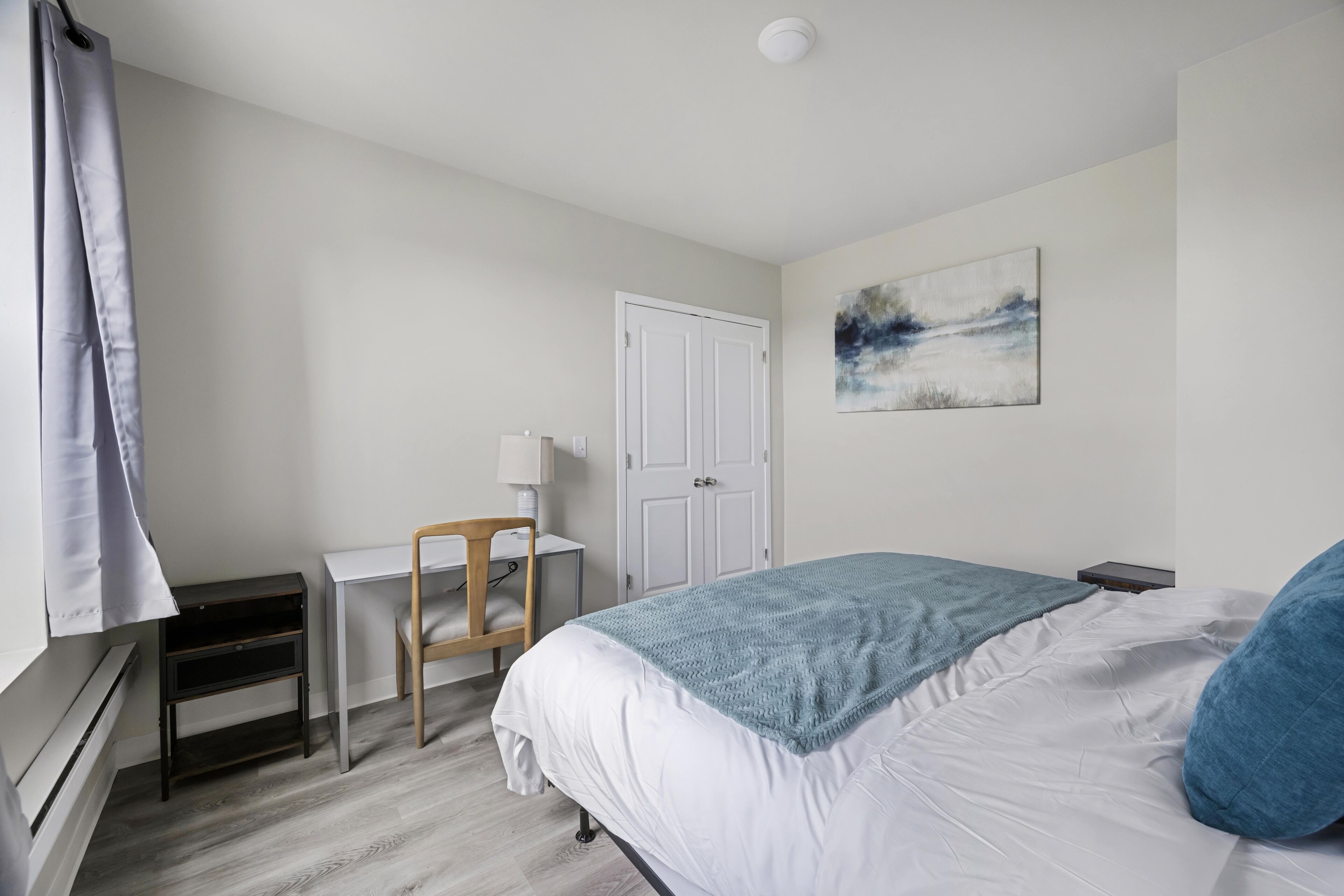 Een slaapkamer met een bed, een bureau, een stoel, een deur en een kunstwerk aan de muur.
