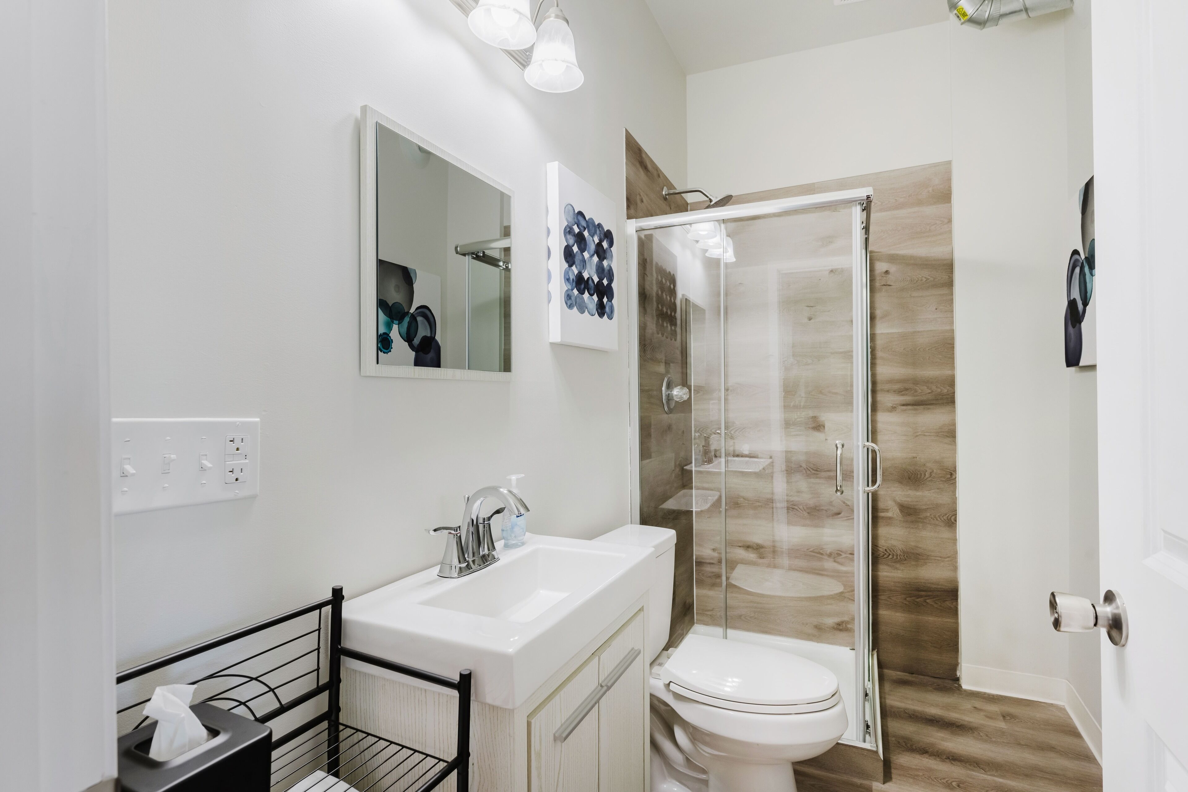 Un baño moderno con cabina de ducha de vidrio, un lavabo blanco con espejo y un inodoro.