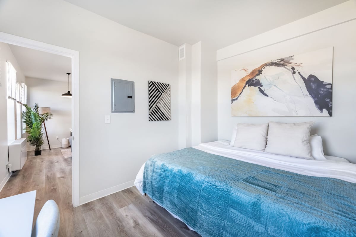 Une chambre à coucher moderne avec un grand lit, une couvre-lit bleue à motifs et un grand tableau abstrait accroché au mur.