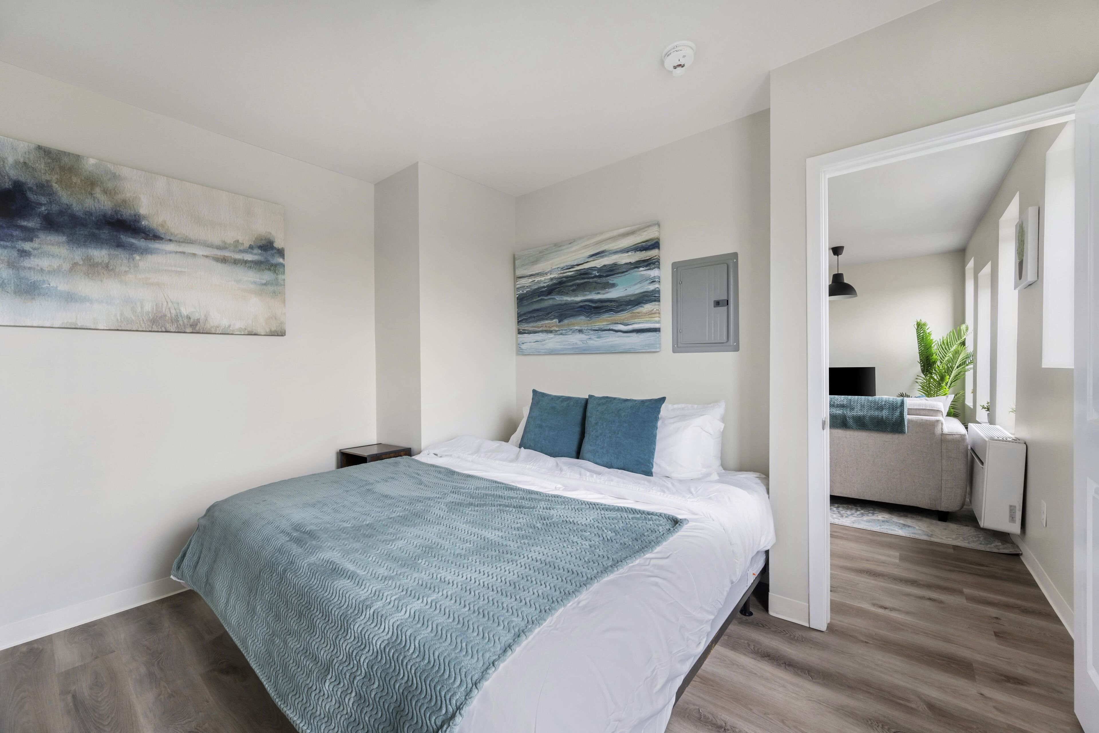 A modern bedroom with a large bed, a view into the living area, and artwork on the walls.
