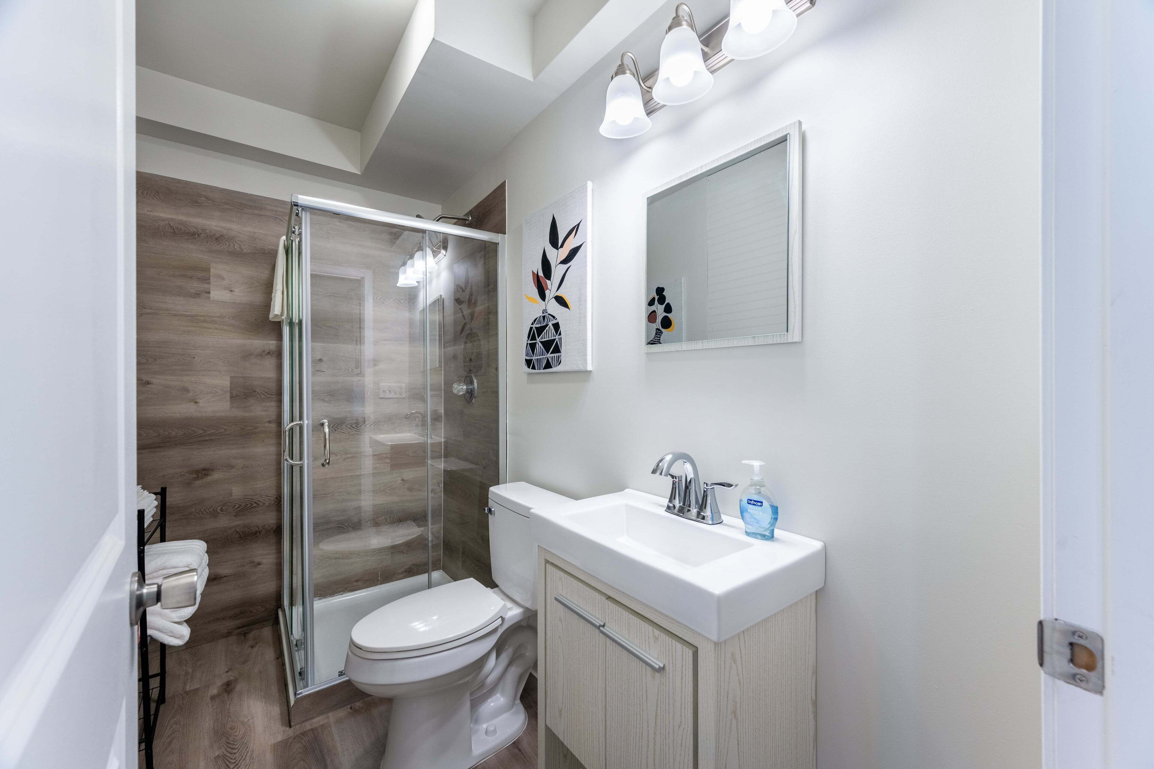 Un bagno moderno con cabina doccia in vetro, un water, un lavandino con specchio e un portascope.