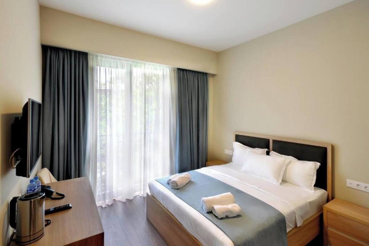 Ein Hotelzimmer mit einem Bett, einem Schreibtisch mit Fernseher, einer Kaffeemaschine und einem Fenster mit Vorhängen.