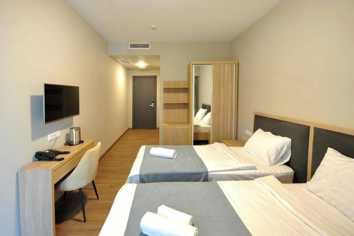 Ein Hotelzimmer mit zwei Betten, einem Schreibtisch mit Computer, einem Fernseher und einem Kleiderschrank.