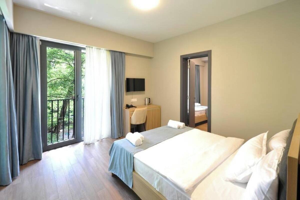 Ein Hotelzimmer mit Bett, Schreibtisch mit Stuhl, Fernseher und einem Balkon mit Vorhängen.