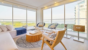 Un salón moderno con un sofá, dos sillones mecedores, una mesa de centro y vistas a zonas verdes a través de grandes ventanales.