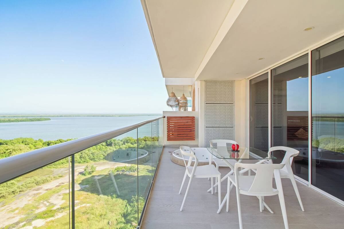A balcony with a glass railing overlooking a body of water and greenery.