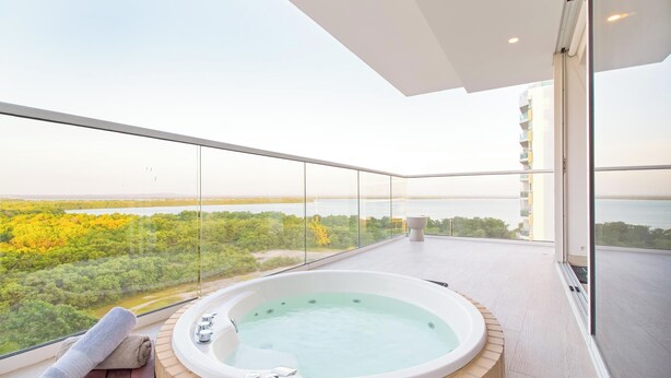 Un balcón con un jacuzzi, una toalla y vistas a un bosque y al agua.