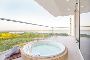 Een balkon met een jacuzzi, een handdoek en uitzicht op bos en water.