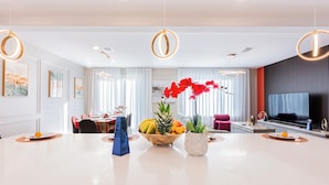 Rebedor d'hotel modern amb una zona de dinning central, una zona de seients amb televisió i un gran finestral amb cortines.