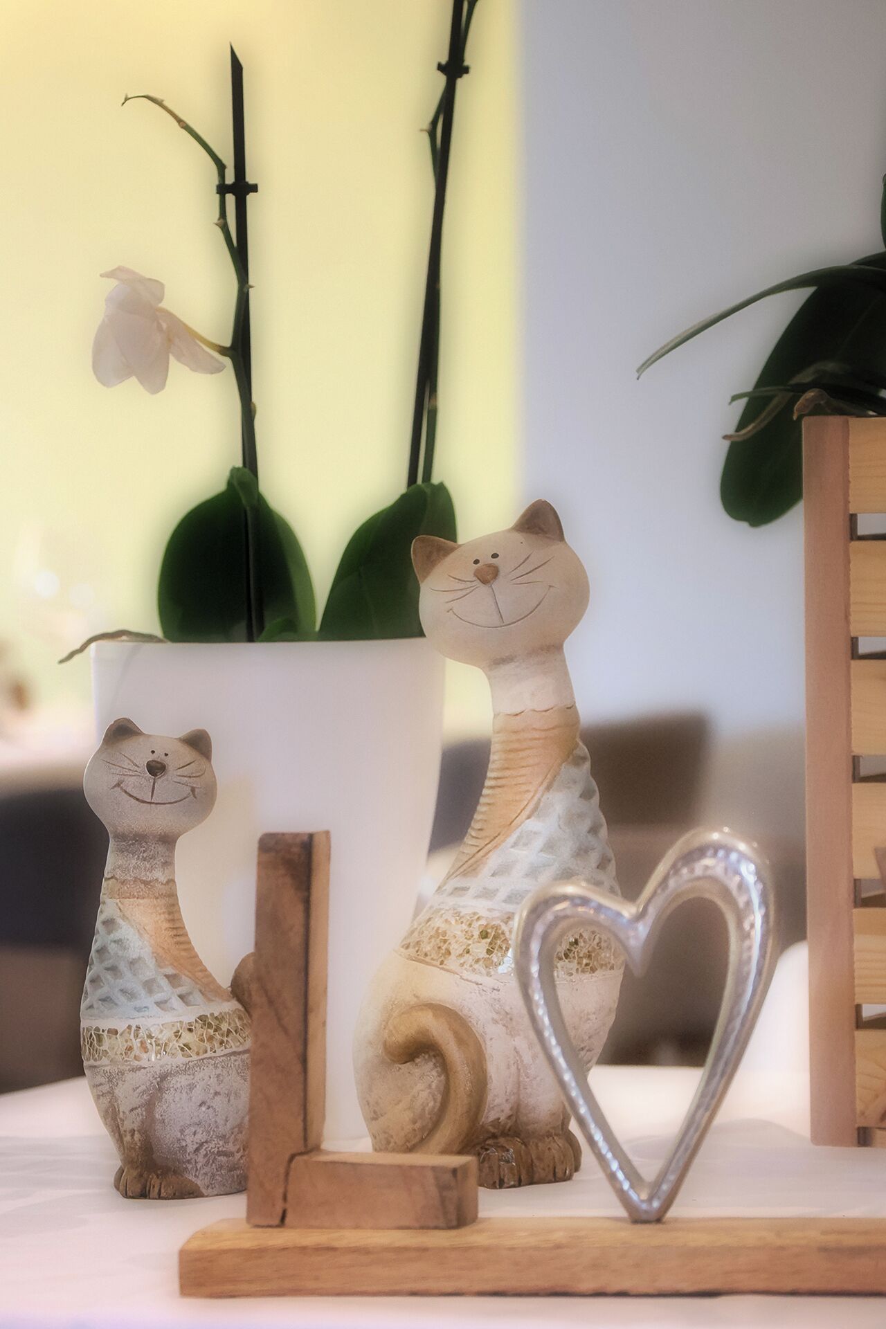 Two ceramic cat figurines on a shelf, a heart-shaped metal ornament, and a potted plant with green leaves.