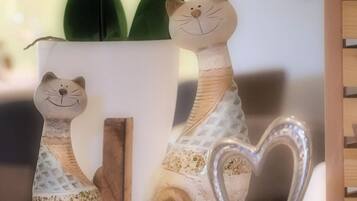Two ceramic cat figurines on a shelf, a heart-shaped metal ornament, and a potted plant with green leaves.