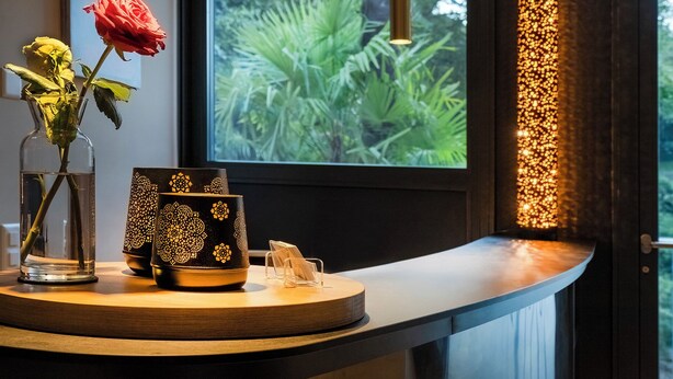 A room with a curved wooden counter, a vase with a red rose, a yellow rose, and a decorative black vase with gold patterns.