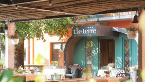 An outdoor cafe with tables and chairs, a sign reading "3e terre", and hanging plants.