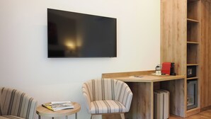 A modern room with a flat-screen TV mounted on the wall, a wooden desk with a coffee machine, and two striped chairs.