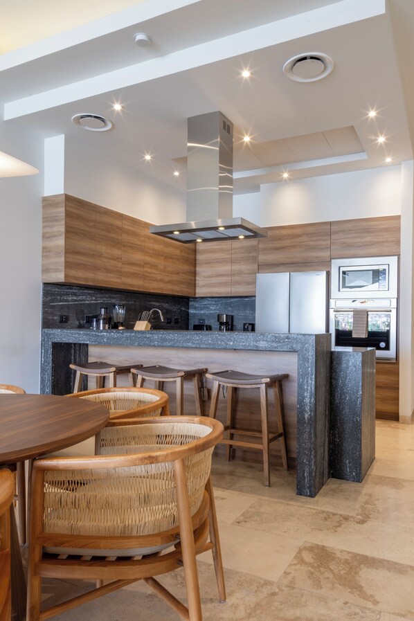 Een moderne keuken met een centraal eiland, barkrukken en een eettafel.