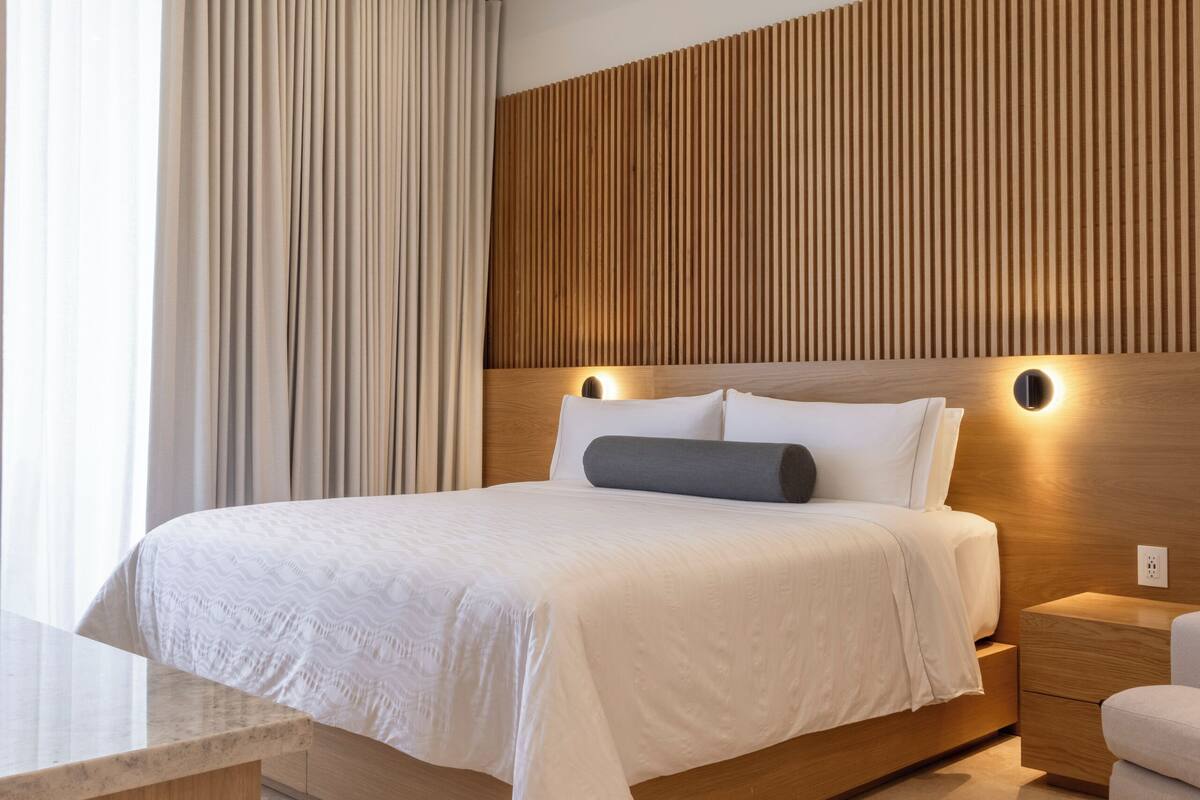 Une chambre d’hôtel moderne avec un grand lit, une tête de lit en bois, une table de chevet et un bureau.