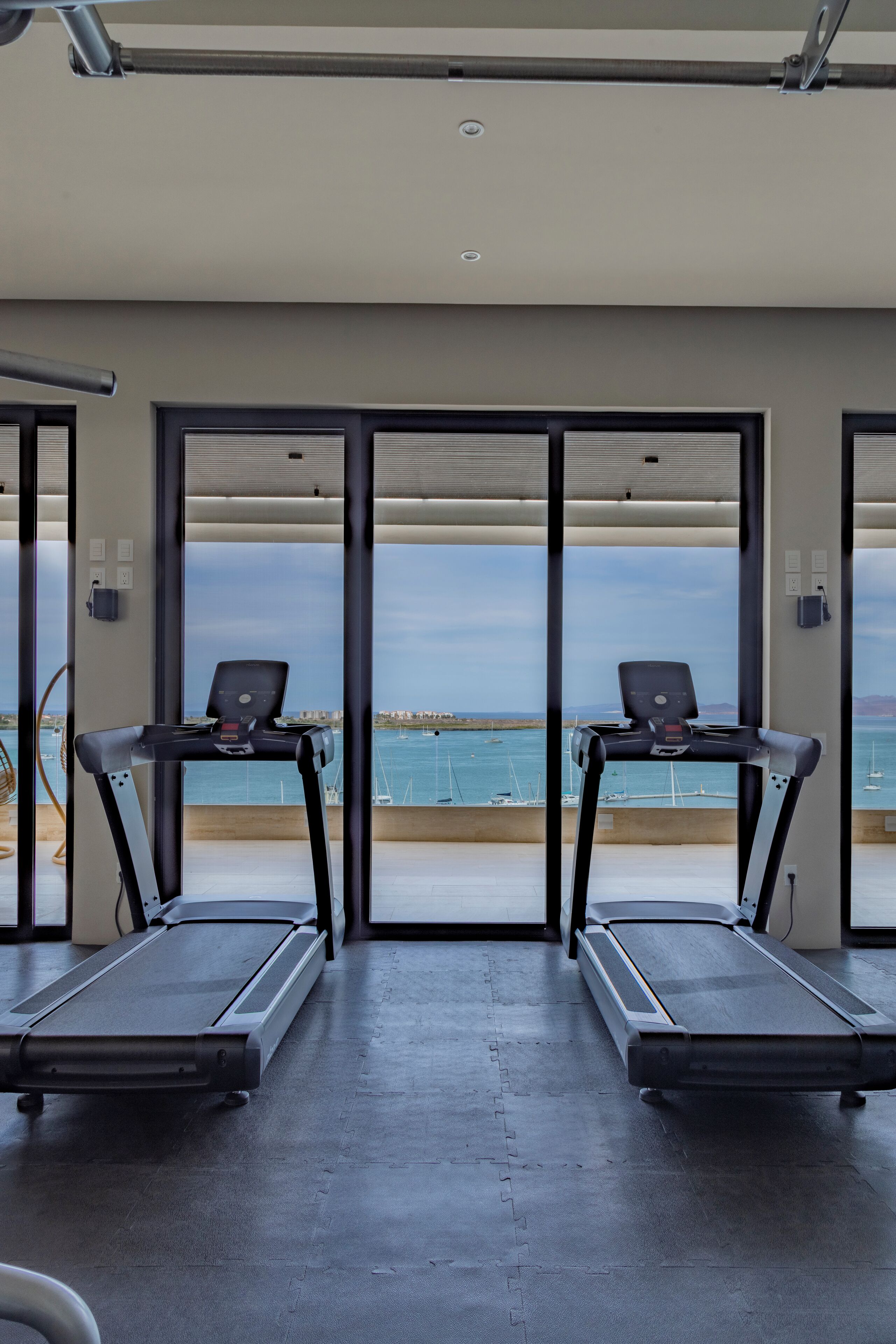 A fitness room with two treadmills facing a scenic view of the sea.