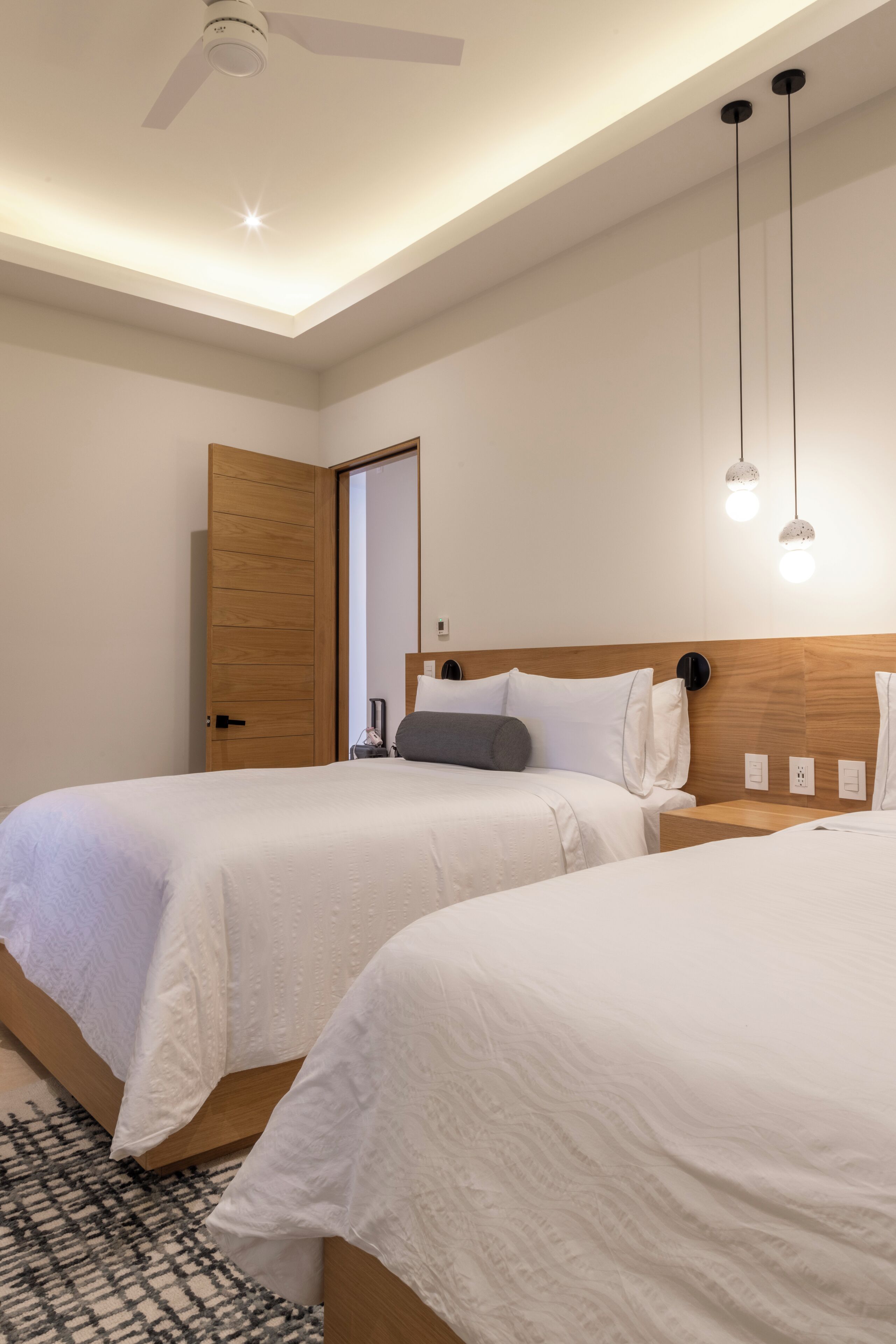 Habitación de hotel con dos camas, ventilador de techo, lámparas colgantes y puerta de madera.