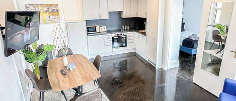 Een moderne keuken met witte kastjes, een eethoek met een houten tafel en stoelen, en een grote spiegel aan de muur.