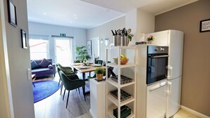 A modern kitchen with a built-in oven and a white refrigerator. There is a dining area with a table and chairs, and a blue rug on the floor.
