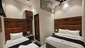 Camera d'albergo con due letti, testiere in legno, una ventola a soffitto, un condizionatore d'aria e un piccolo comodino con una bottiglia d'acqua.