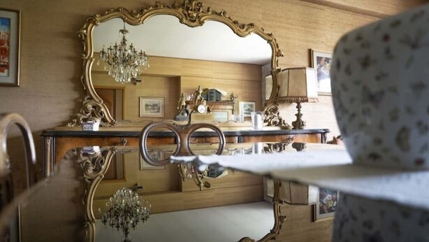 Una habitació amb un mirall gran i decoratiu que reflecteix una làmpada de cristall i un armari de fusta.