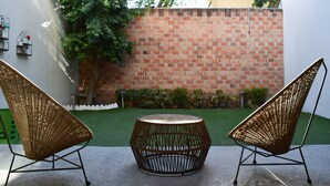 A patio with two wicker chairs and a round table, a brick wall, and a small garden area.