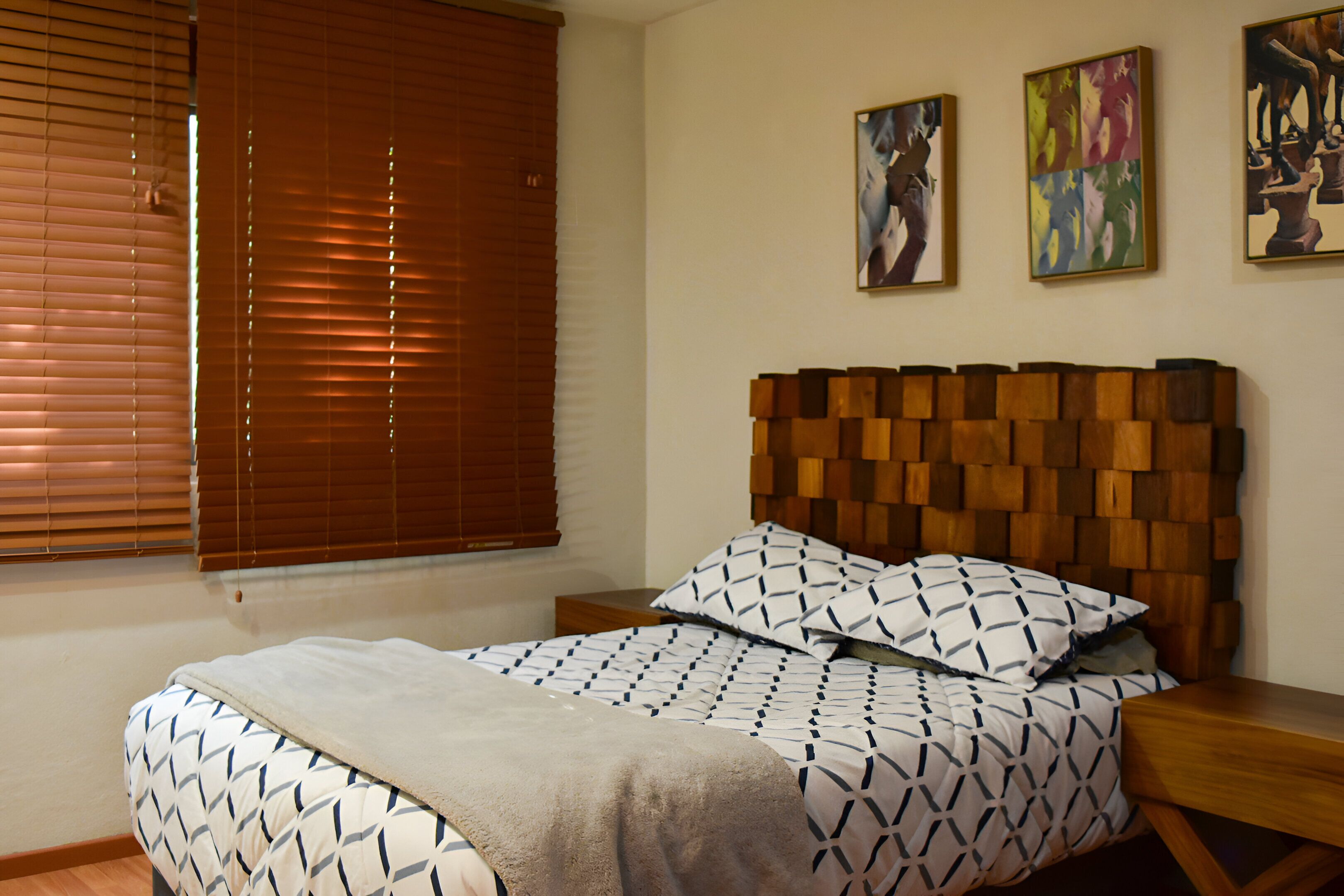 A bedroom with a wooden headboard, patterned bedding, and artwork on the wall.