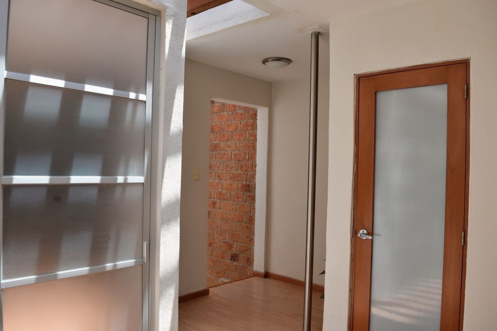A hallway with a brick wall, a wooden door, and a metal-framed window.