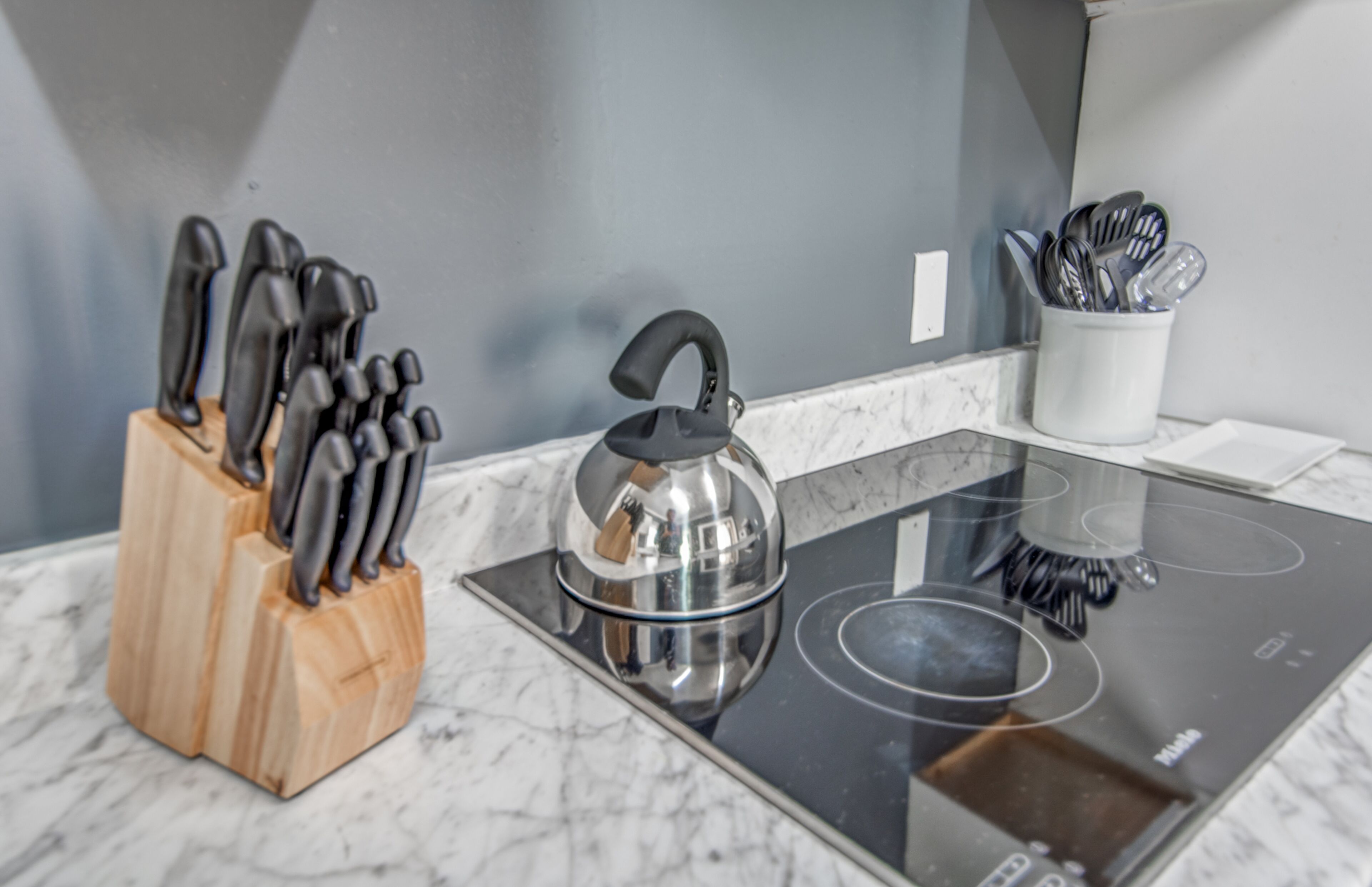 A kitchen with a wooden knife block, a kettle, and a cup of utensils on a countertop.
