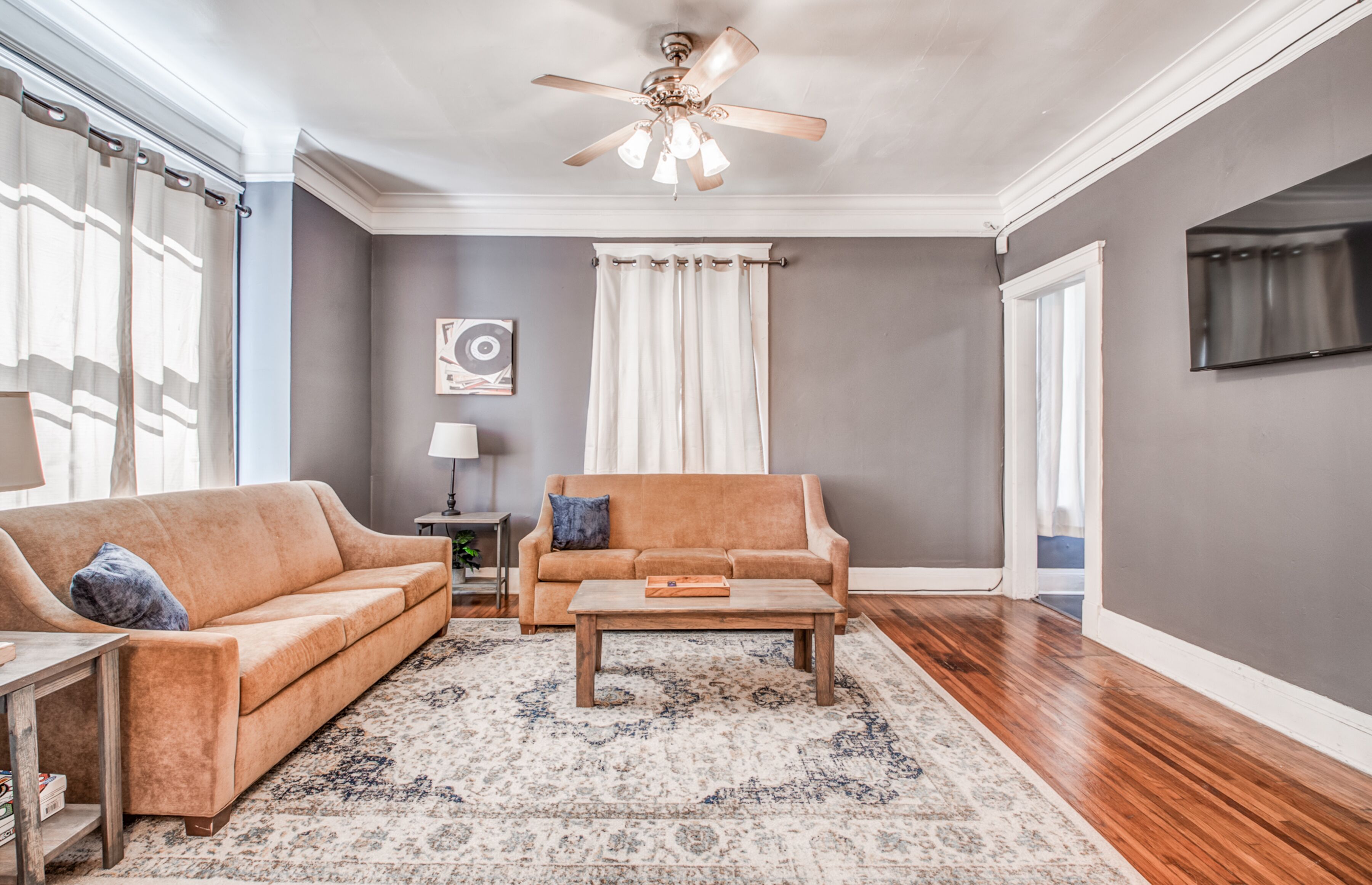 A living room with two sofas, a coffee table, a ceiling fan, and a TV mounted on the wall.