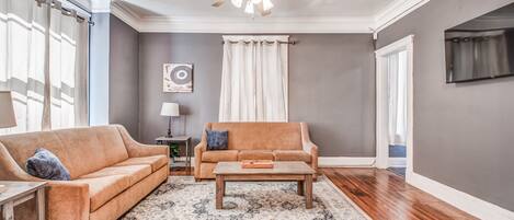 A living room with two sofas, a coffee table, a ceiling fan, and a TV mounted on the wall.