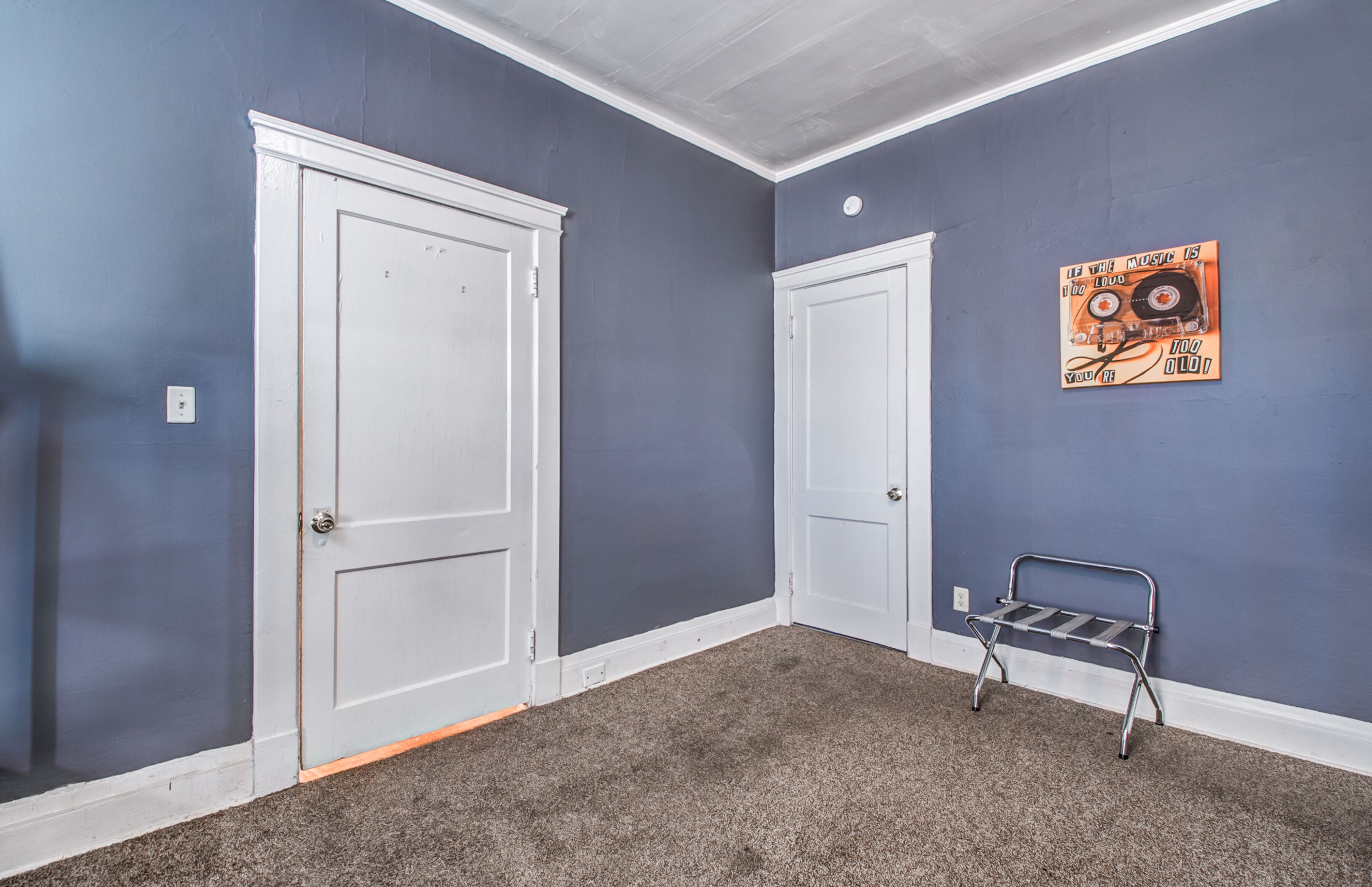 A room with two white doors, a grey carpet, and a metal bench.