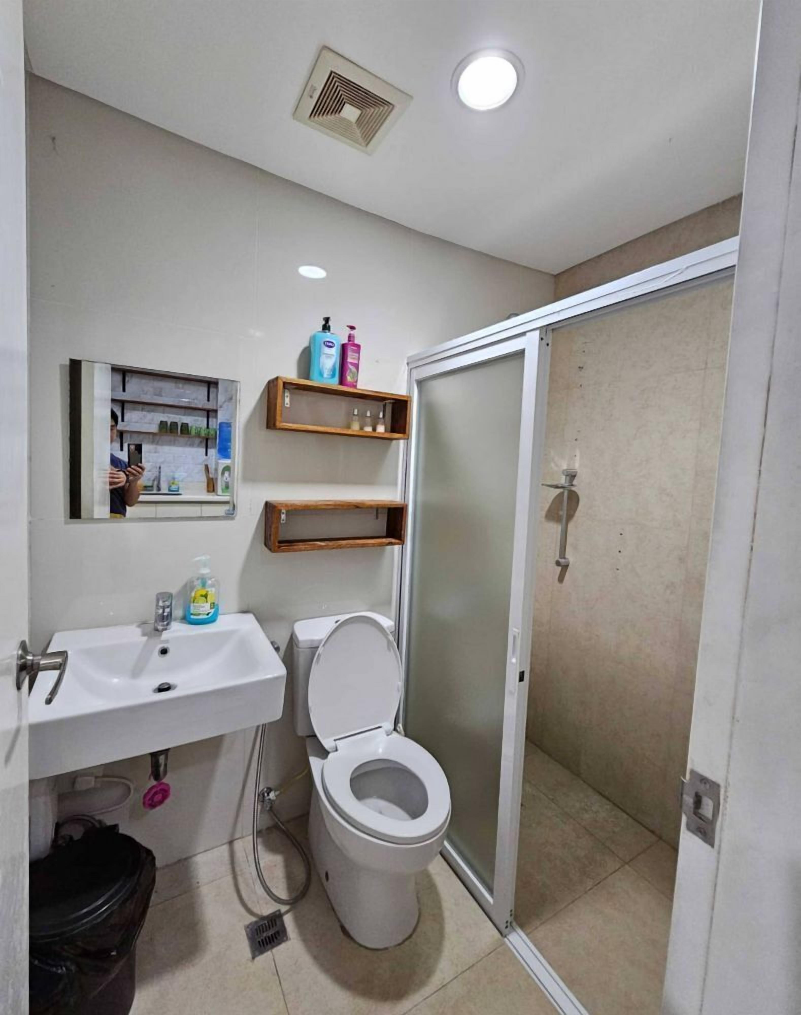 A bathroom with a toilet, sink, and shelves with toiletries.