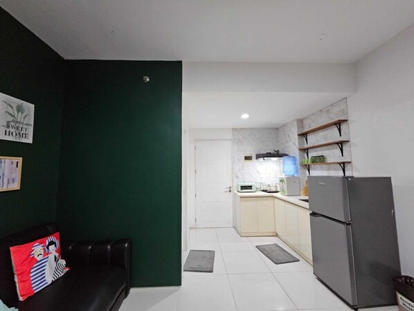 A modern kitchen with a refrigerator, microwave, and sink. There is a dark green wall and a white door leading to another room.