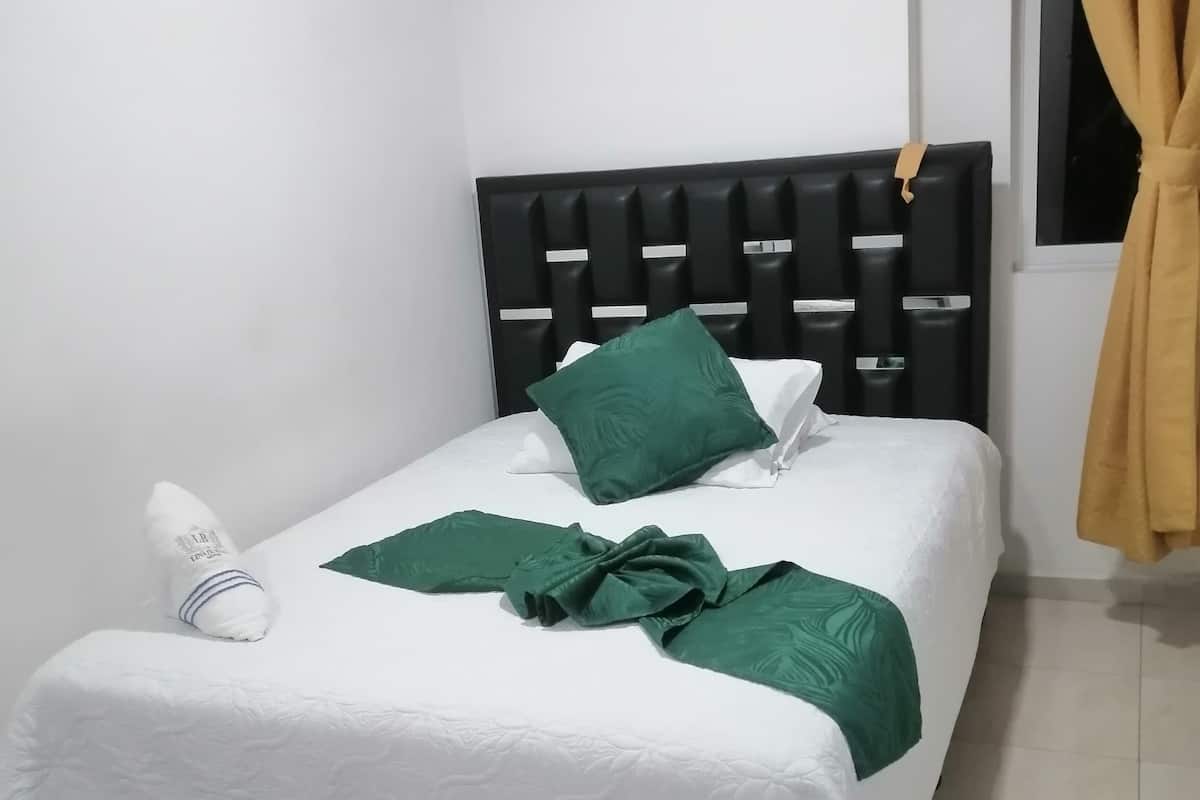 A neatly made bed with a white bedspread and green pillows, a black headboard, and a window with curtains.
