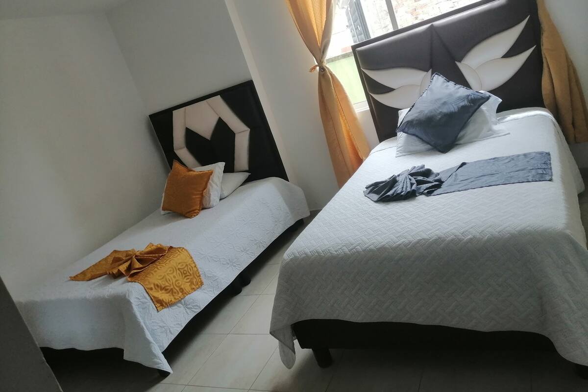 Two single beds with headboards, a window with curtains, and a view of a brick building outside.
