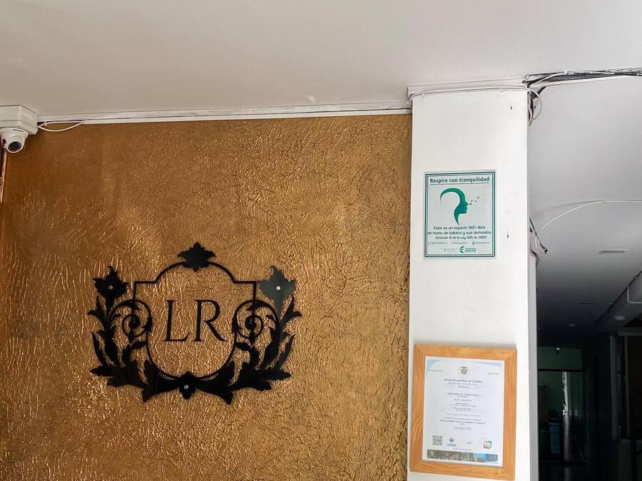 En receptionsdisk med en vägg som har en guldfärgad, strukturerad yta, en övervakningskamera och diverse föremål som en vattenflaska, nycklar och ett anteckningsblock.