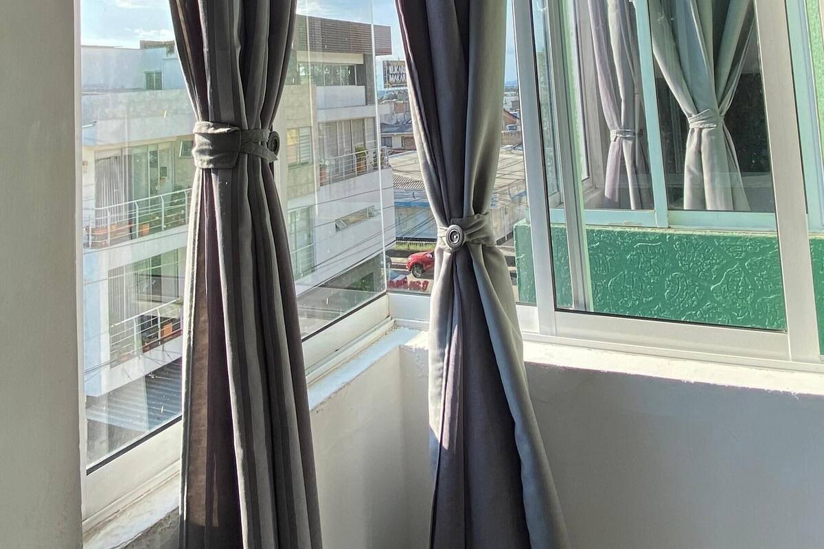 A room with a window featuring grey curtains tied back, revealing a cityscape view.