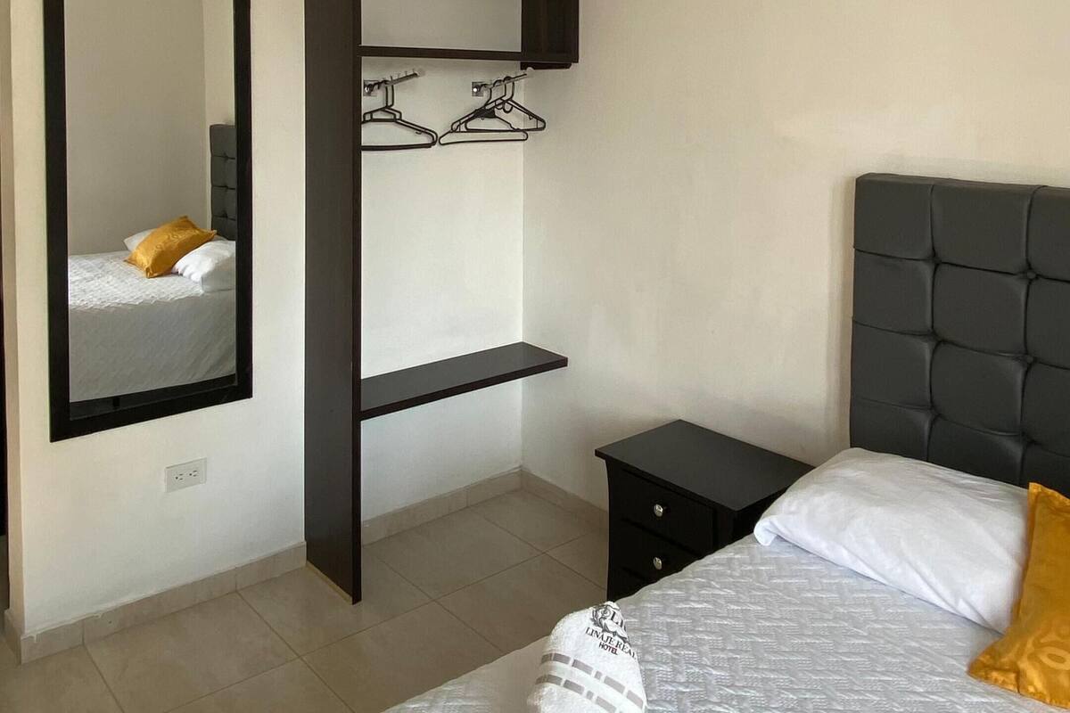 A hotel room with a bed, a mirror, a wardrobe, and a nightstand.
