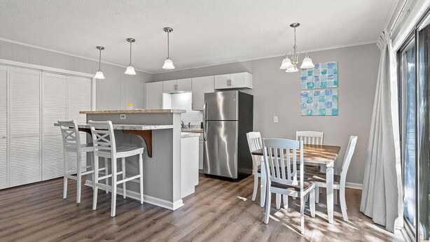 A modern kitchen with white cabinetry, a stainless steel refrigerator, and pendant lighting. - Havens by the Sea STE A Cozy 2BR Beachside Escape (North Myrtle Beach)
