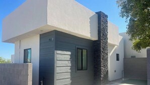 Une maison moderne à deux étages, avec une façade grise, un mur d’accent en pierre et un numéro de maison bien visible.
