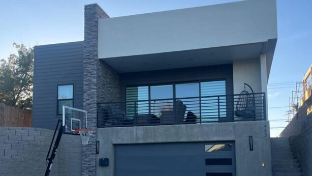Une maison moderne à deux étages, dotée d’un garage, d’un panier de basketball et d’une allée en béton.